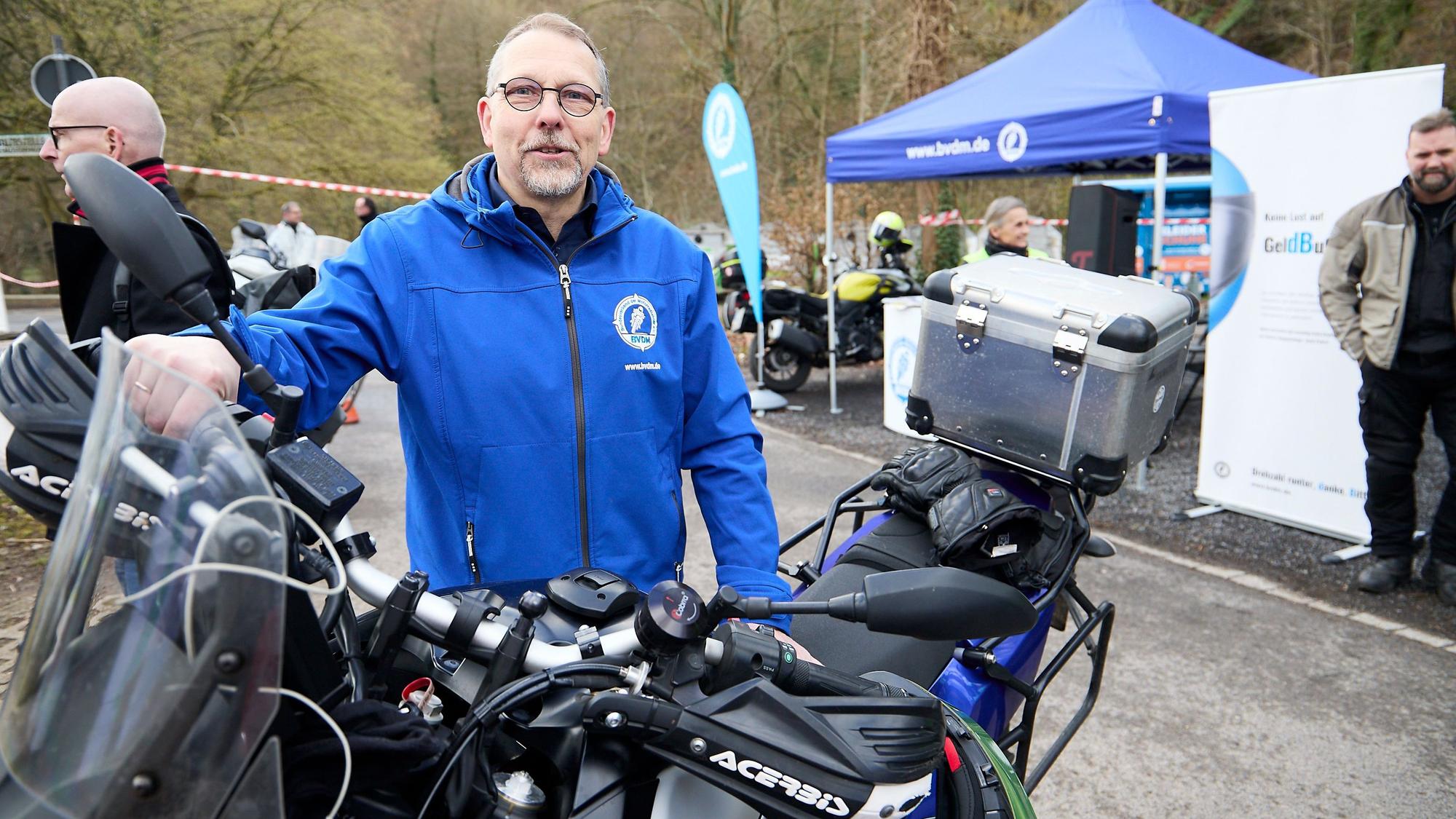 Michael Lenzen an einem Motorrad, im Hintergrund Infostände.