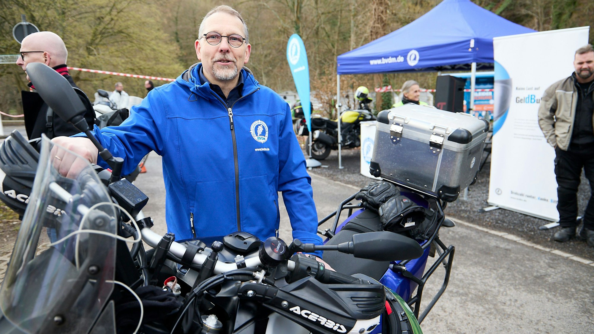 Michael Lenzen an einem Motorrad, im Hintergrund Infostände.