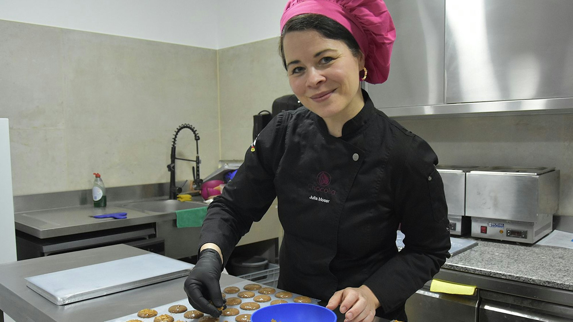 Zu sehen ist eine Frau in ihrer Schokoladenmanufaktur, auf dem Tisch liegen verschiedene Pralinen.