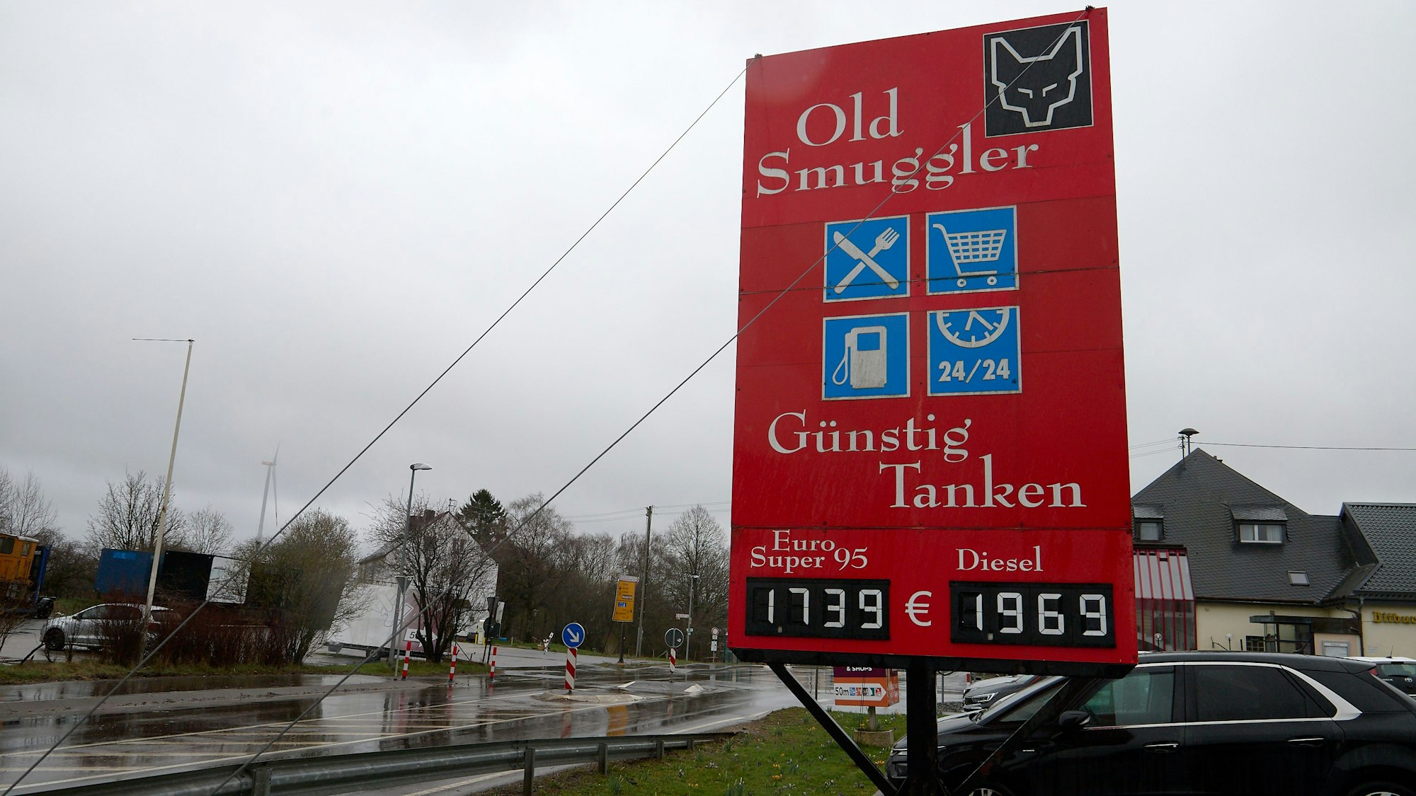 An einer Straße steht ein rotes Schild, auf dem Benzinpreise angezeigt werden.