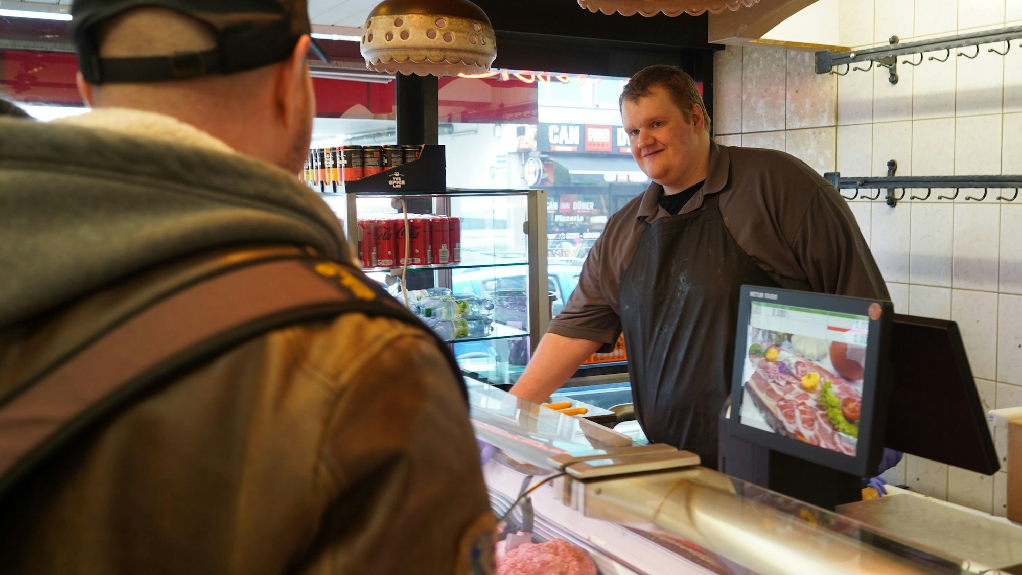 Das Foto zeigt einen Mann, der einem Kunden Fleisch in einer Metzgerei verkauft.