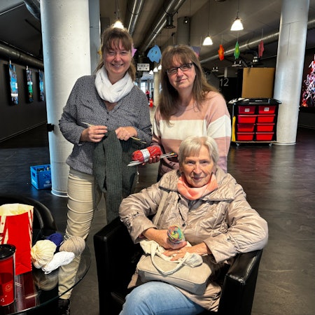 Die Schwestern stehen hinter ihrer Mutter, die in einem Sessel im Foyer sitzt.