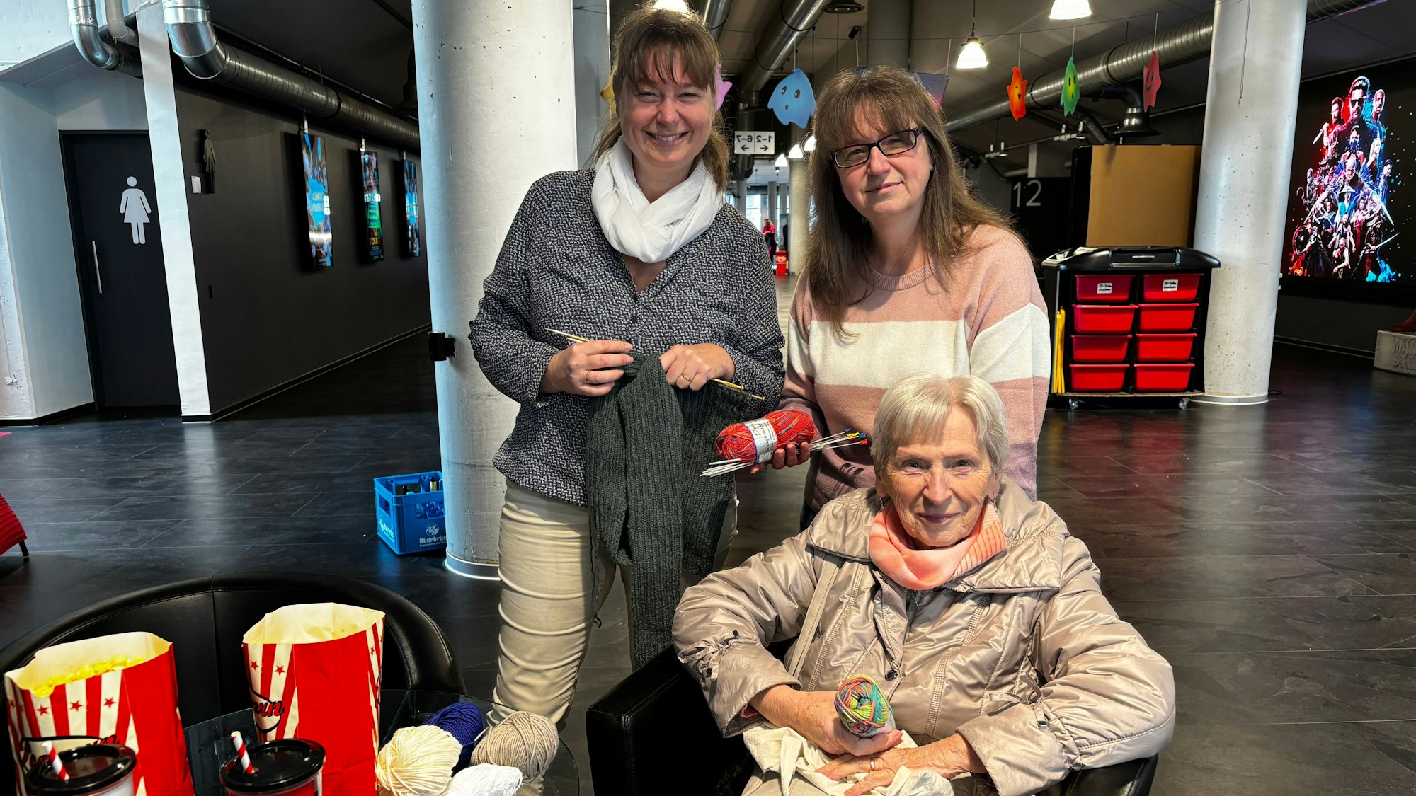 Die Schwestern stehen hinter ihrer Mutter, die in einem Sessel im Foyer sitzt.