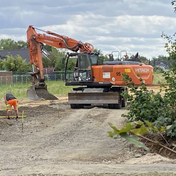 Zu sehen sind Bauarbeiter und ein Bagger auf einer Baustelle.