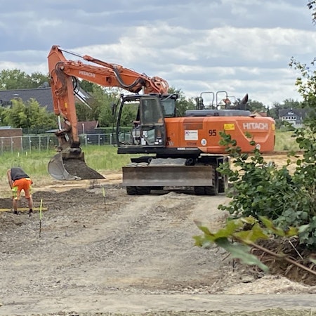 Zu sehen sind Bauarbeiter und ein Bagger auf einer Baustelle.