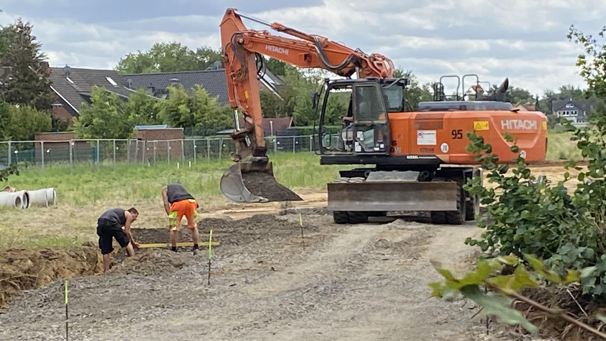 Zu sehen sind Bauarbeiter und ein Bagger auf einer Baustelle.