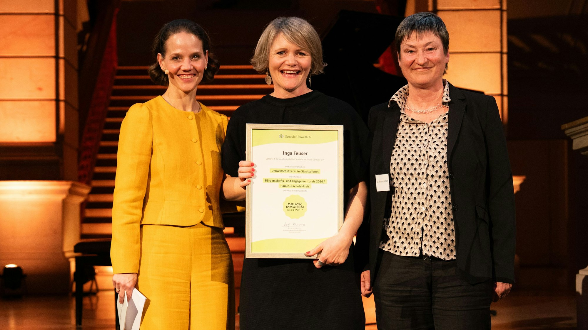 Drei Frauen lächeln in die Kamera, Inga Feuser (Mitte) hält eine Urkunde in den Händen.