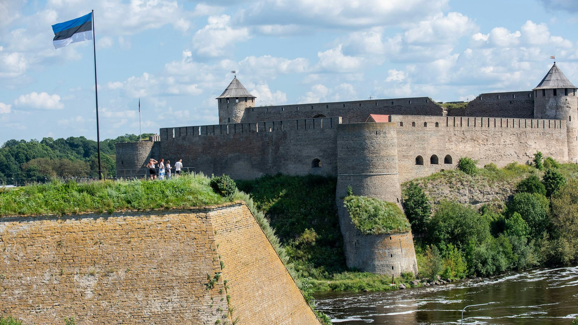 Die estnische Flagge weht über Touristen in Narva, während diese auf die Ivangorod-Festung auf der gegenüberliegenden Flussseite blicken. Die Stadt liegt an der östlichen Grenze Estlands und wird durch den Fluss Narva geteilt. Sie ist die drittgrößte Stadt des Landes und überwiegend russischsprachig. (Archivbild)