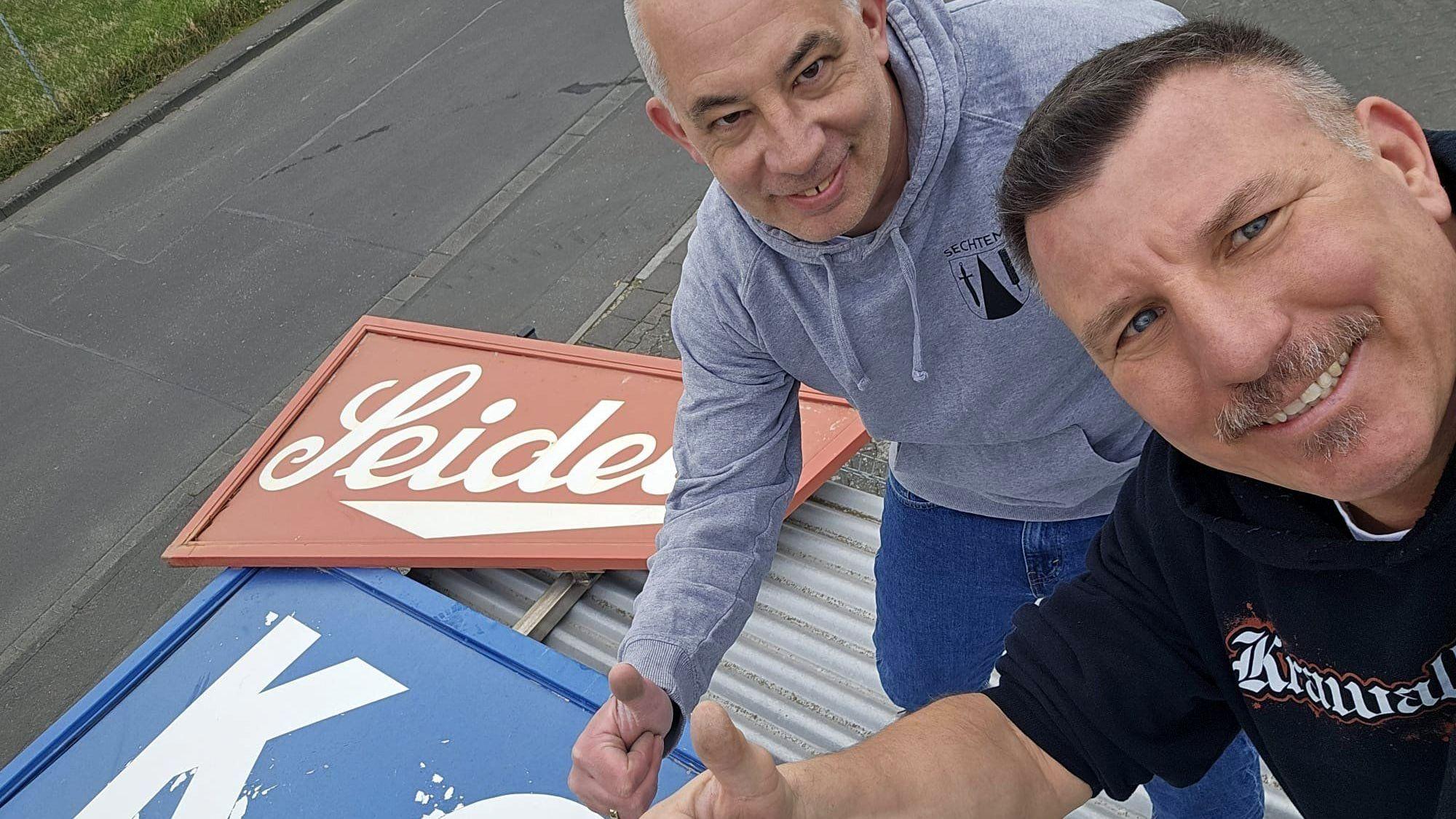 Andreas Geuer (links) und Oli Wirtz mit dem Firmenschild.