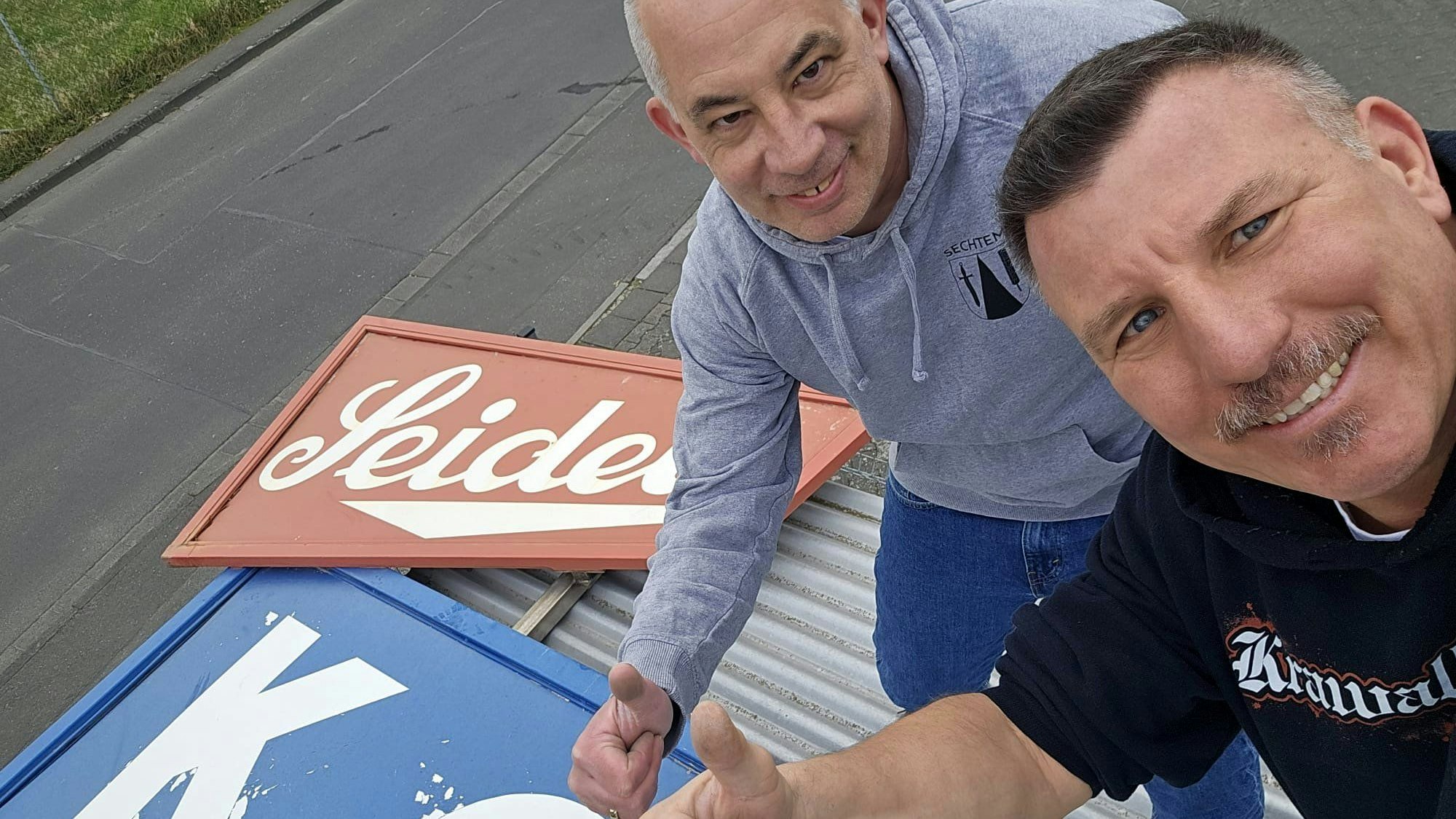Andreas Geuer (links) und Oli Wirtz mit dem Firmenschild.