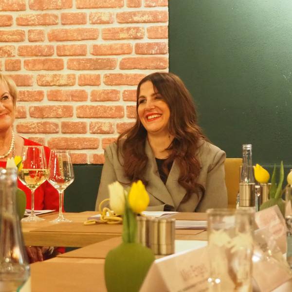 Bernadette Hein (l.) und Judith Kneuttinger sitzen an einem Tisch mit Weingläsern und Blumen darauf.