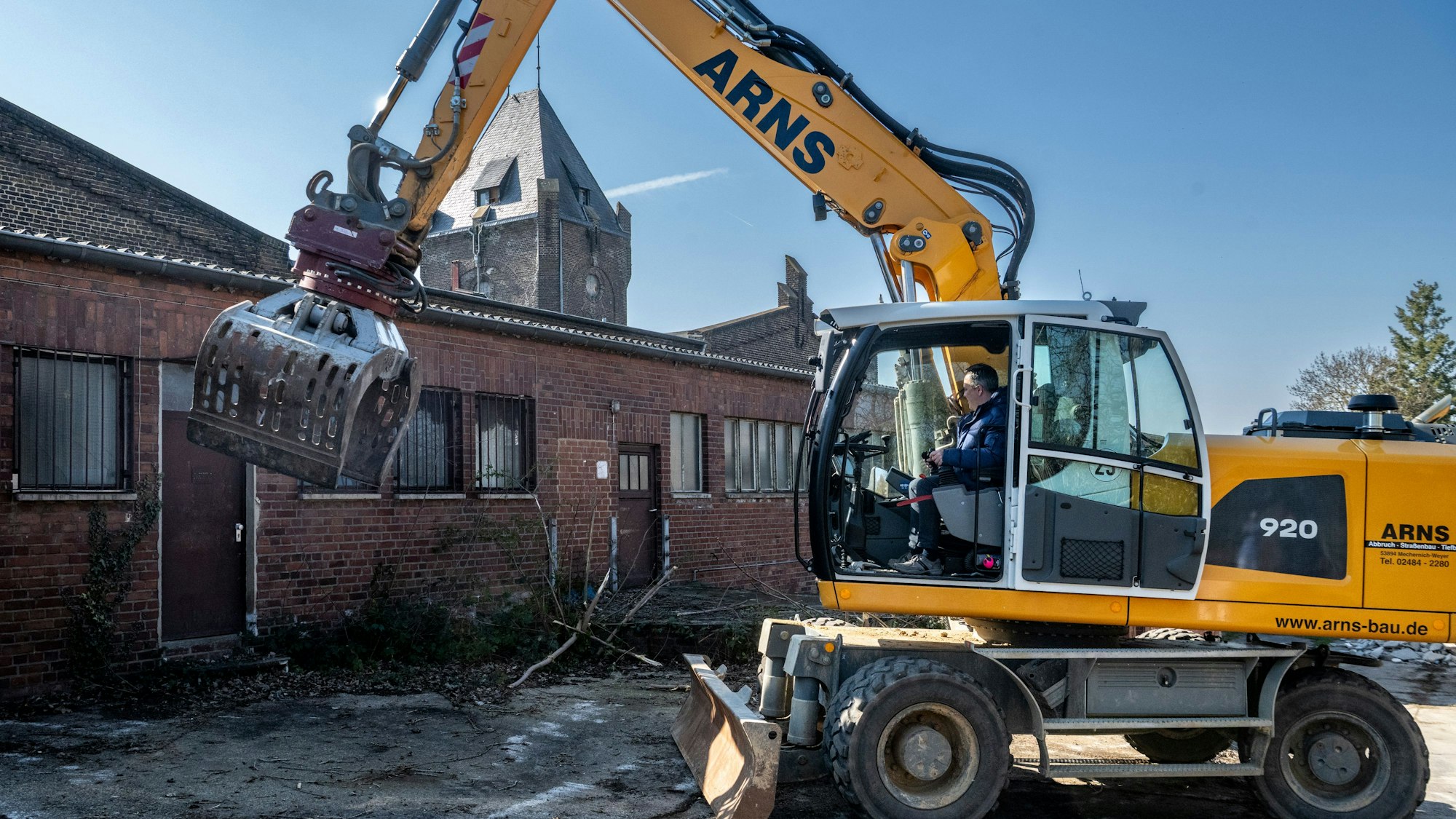 Das Bild zeigt Bürgermeister Sacha Reichelt in einem Bagger. Er reißt ein Fenster ein.