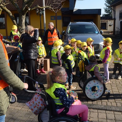 Kinder in Warnwesten und mit gelben Kappen, einige Kinder sitzen im Rollstuhl.