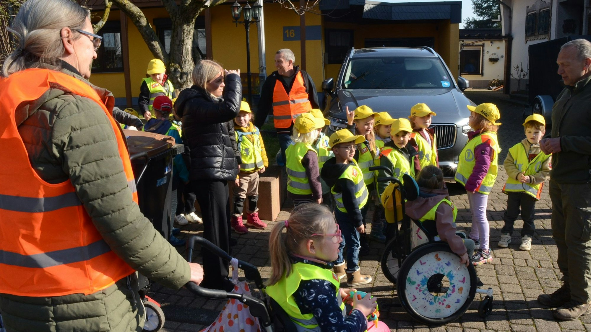 Kinder in Warnwesten und mit gelben Kappen, einige Kinder sitzen im Rollstuhl.