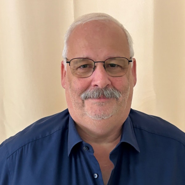 Auf dem Bild ist das Portrait eines Mannes mit Brille und in einem blauen Hemd zu sehen.