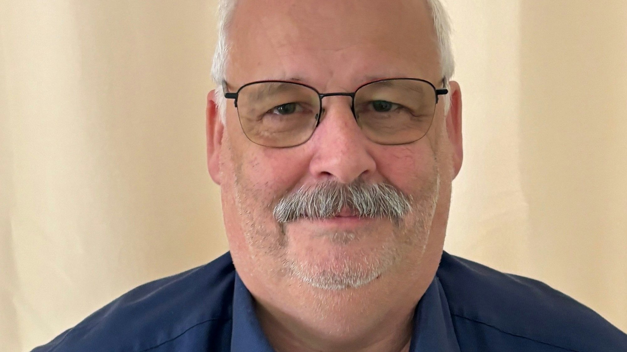 Auf dem Bild ist das Portrait eines Mannes mit Brille und in einem blauen Hemd zu sehen.