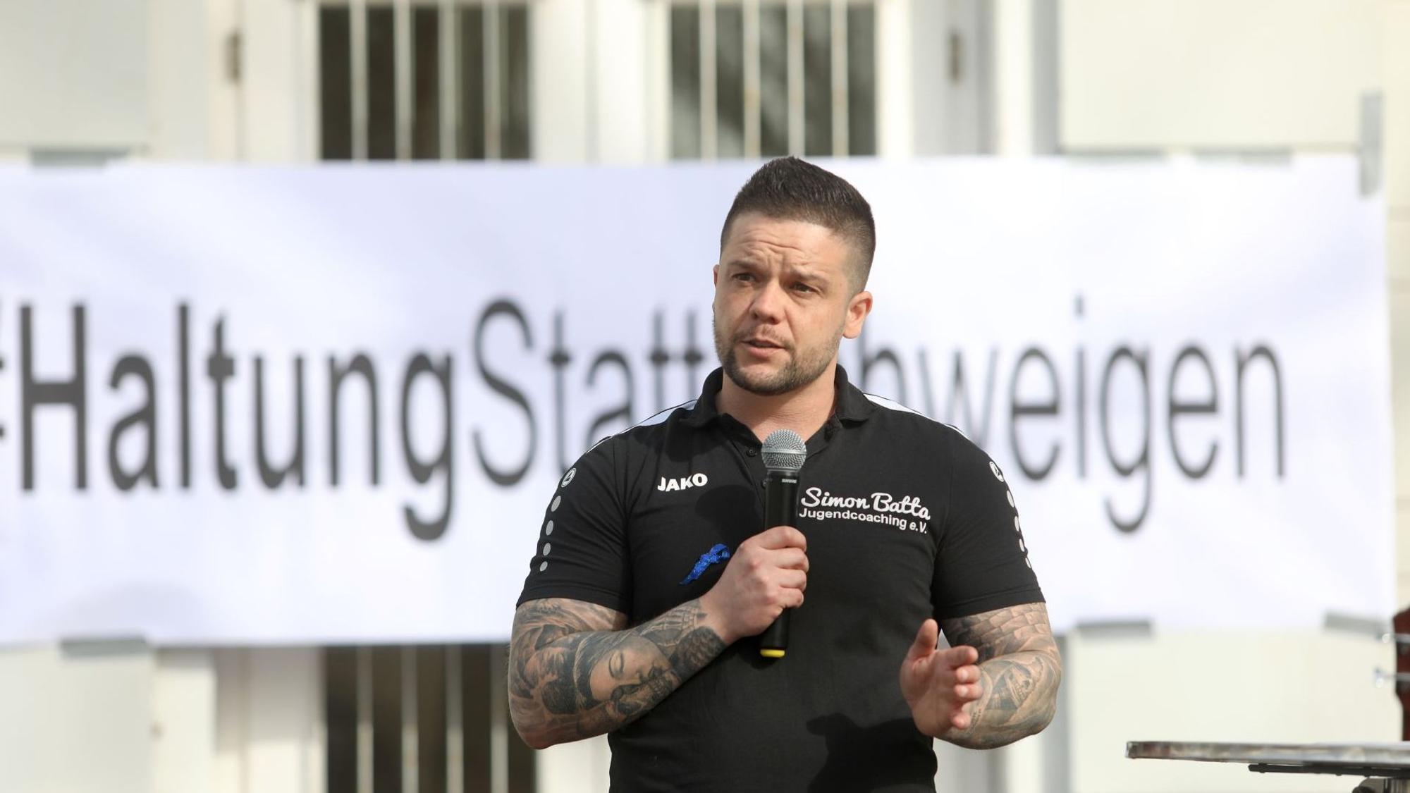 Ein Mann mit Mikrofon, im Hintergrund ein Transparent „Haltung statt Schweigen“.