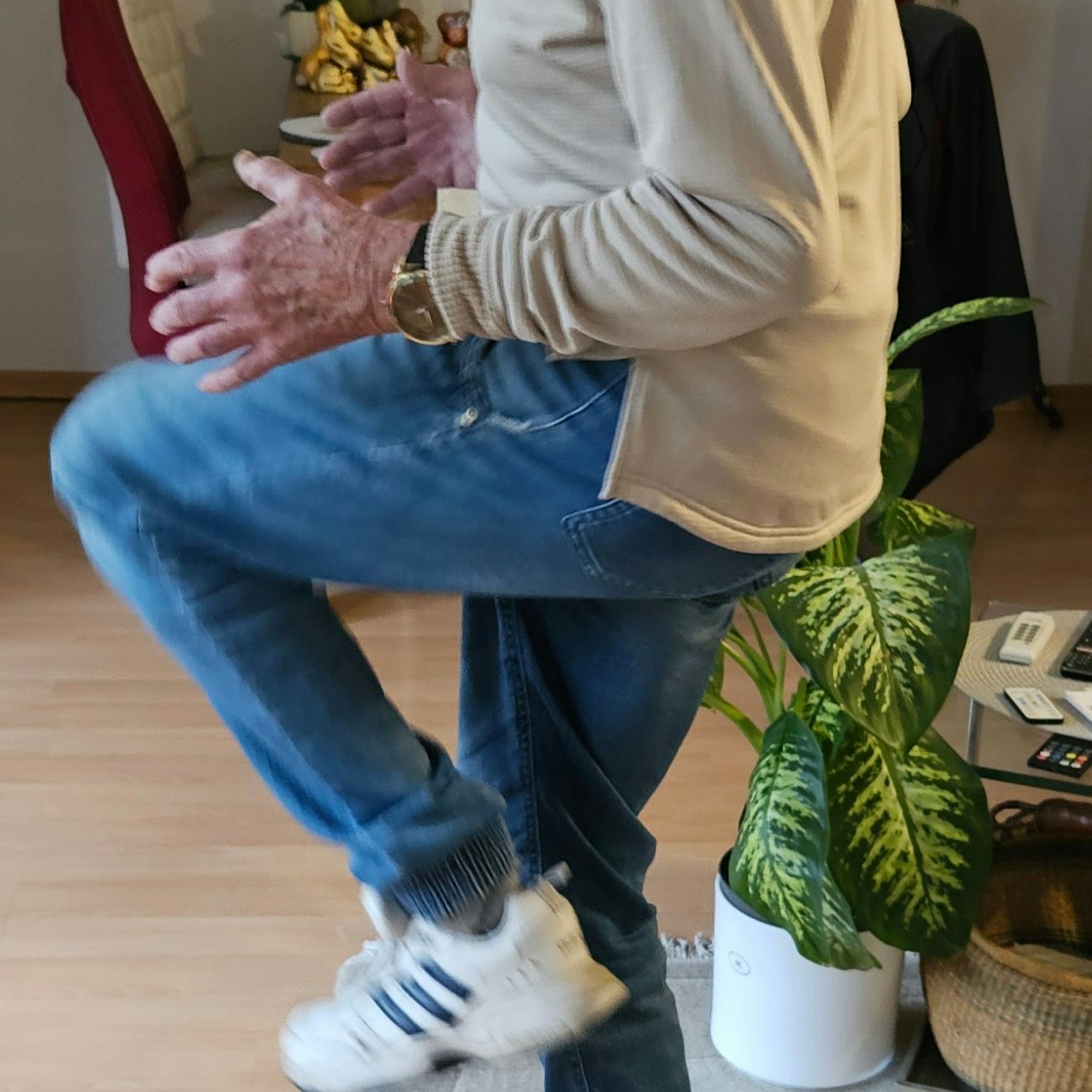 Ein Senior hebt im Stand dei Knie auf Bauchhöhe.