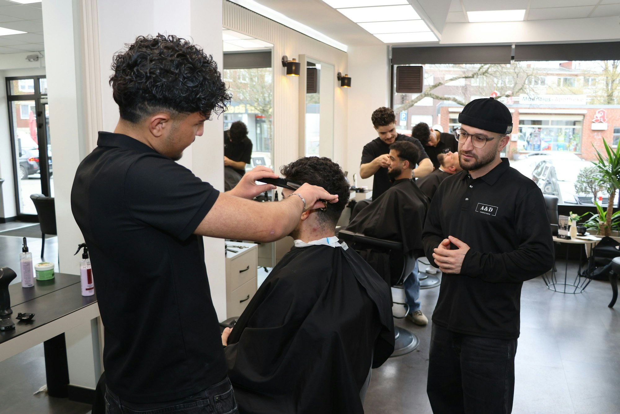 Auf dem Bild sind der Inhaber und Mitarbeiter eines Friseursalons zu sehen.