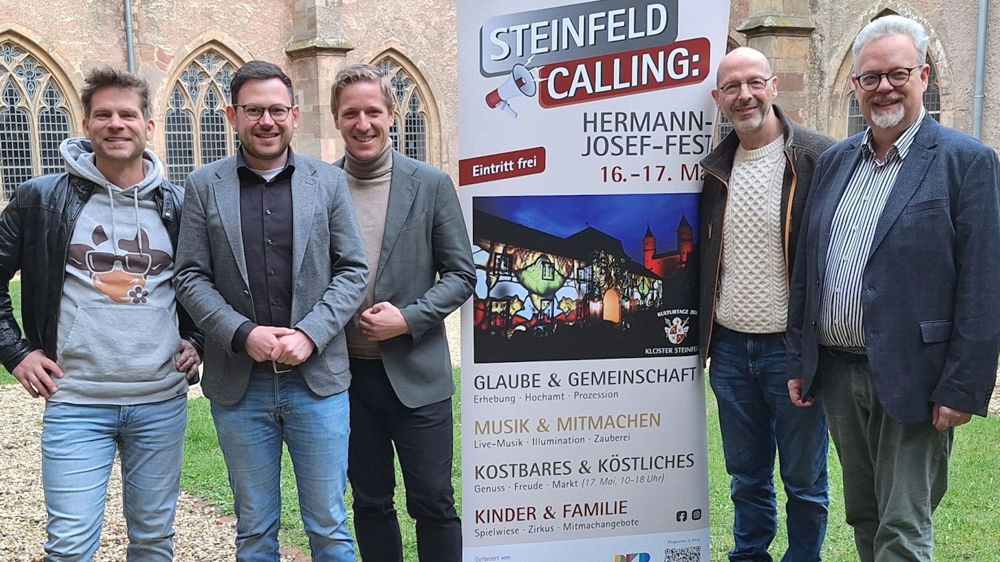 Die Obengenannten stehen vor der Basilika, zwischen ihnen wird auf einem Aufsteller für Steinfeld Calling geworben.