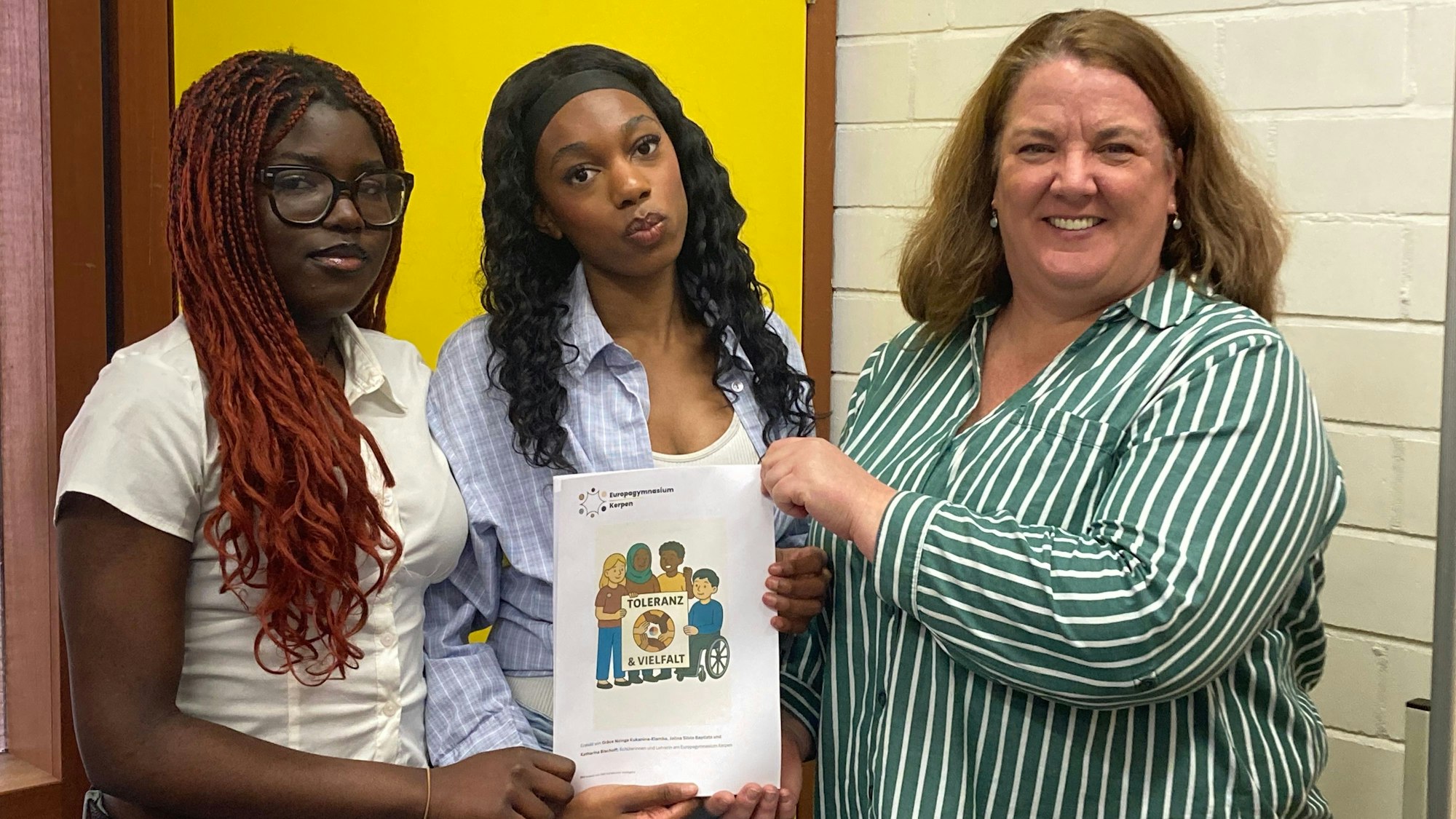 Zu sehen sind zwei jugendliche Mädchen und eine Frau, die eine Mappe halten.