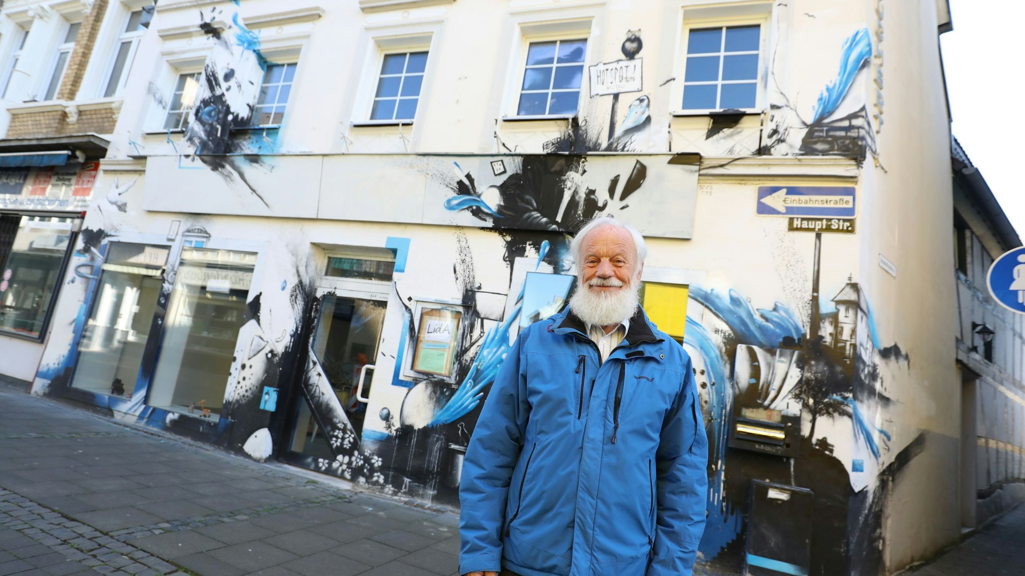 Ein Mann in blauer Jacke vor einem Haus, dessen Fassade mit Graffiti gestaltet ist.