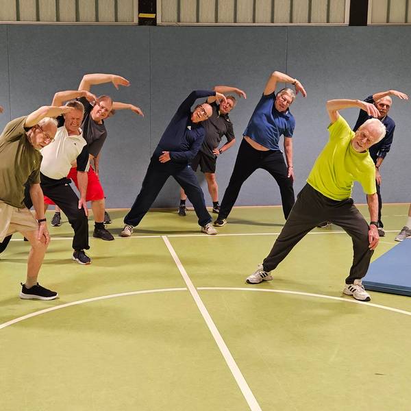 Eine Gruppe von älteren Männern macht Dehnübungen in einer Sporthalle.