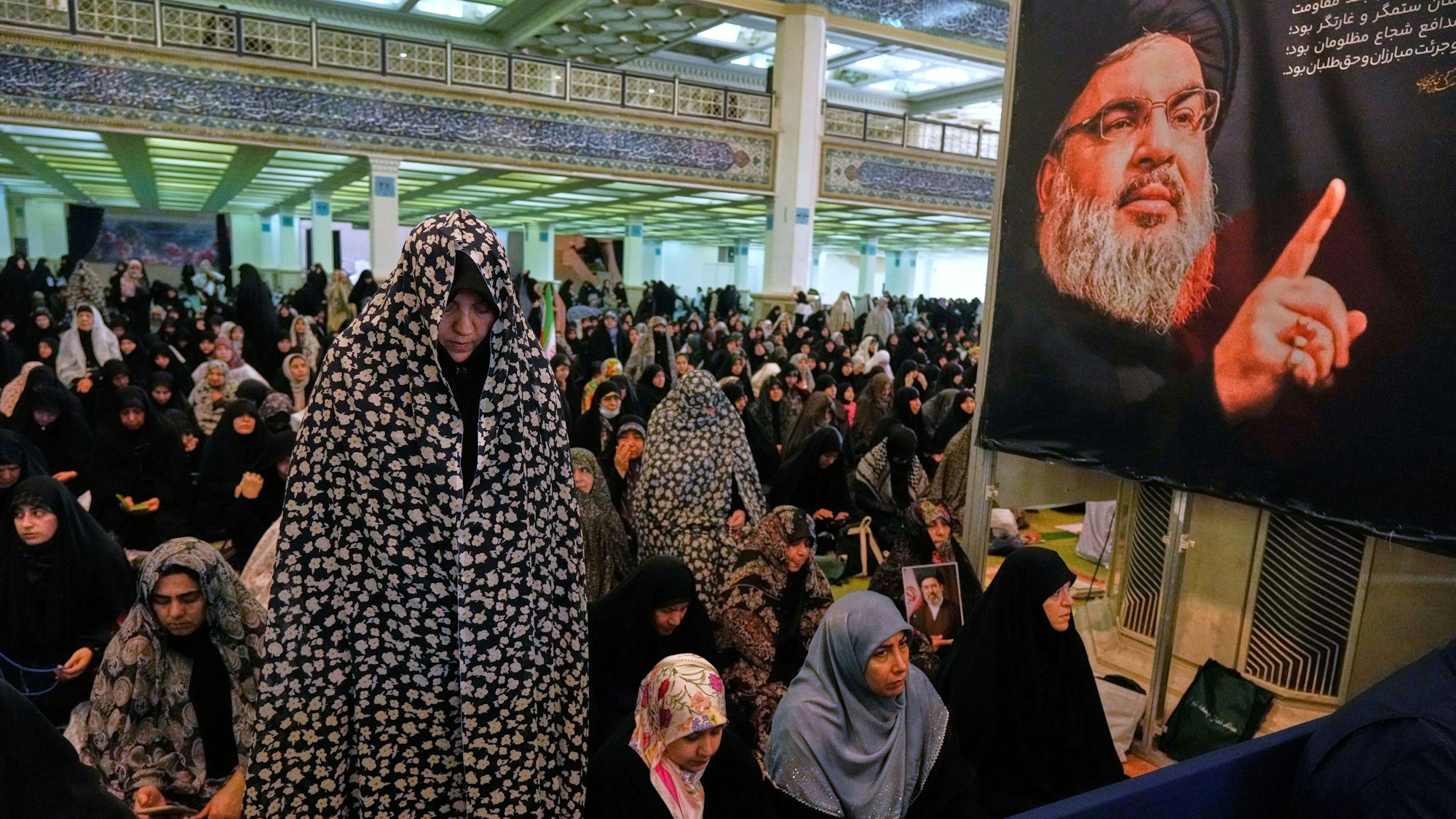 Eine iranische Gläubige betet während einer Zeremonie zum Eid al-Fitr-Gebet, das das Ende des heiligen Fastenmonats Ramadan markiert, während rechts ein Porträt des getöteten libanesischen Hisbollah-Führers Hassan Nasrallah zu sehen ist.