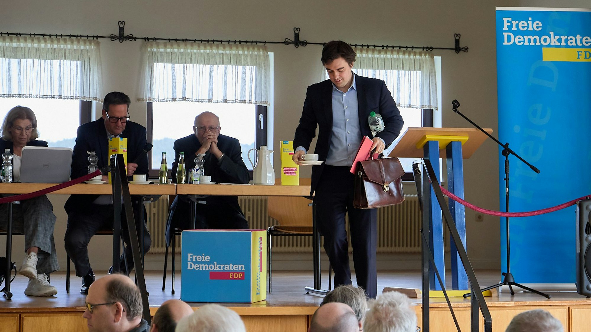 Frederik Schorn verlässt mit der Kaffeetasse in der einen und der Aktentasche in der anderen Hand die Bühne. Links vom ihm sitzen Präsidiumsmitglieder, im Vordergrund Besucher des Parteitags.