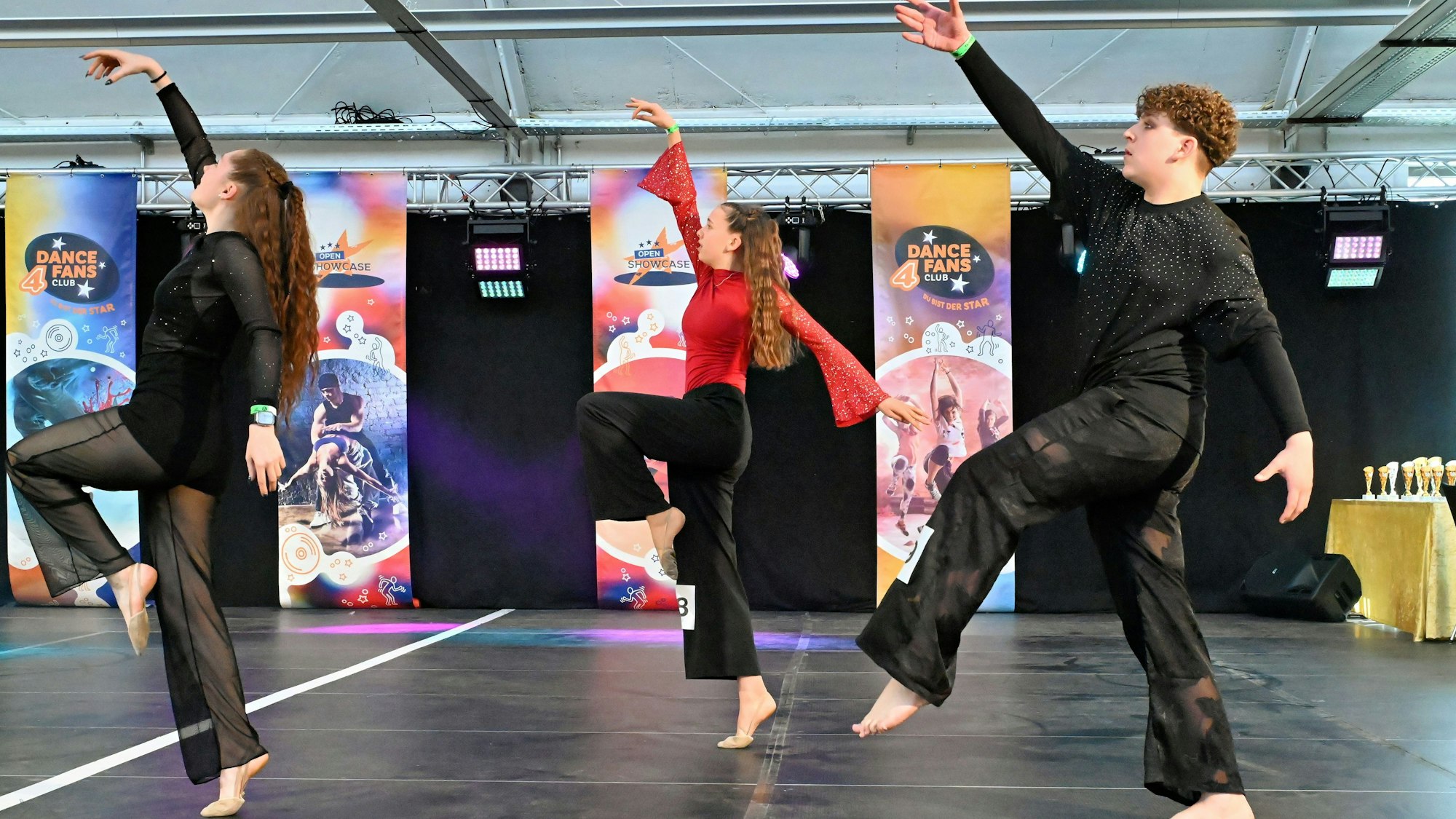 Drei Jugendliche tanzen augf einer Bühne, zwei sind ganz in Schwarz gekleidet, eine trägt ein rotes Oberteil.