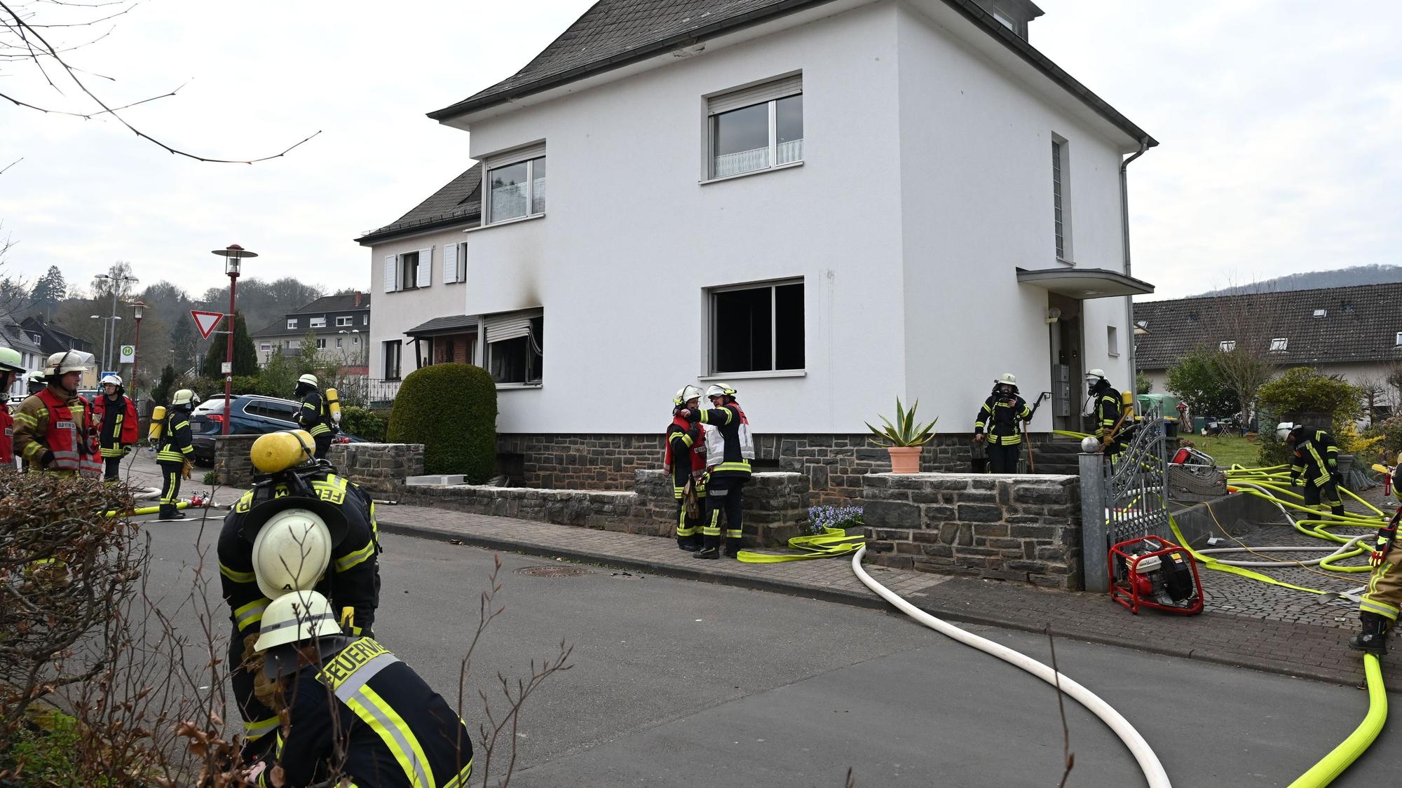 Feuerwehrleute haben Schläuche zu einem Haus verlegt. An einem Fenster sind Rauchspuren zu sehen.