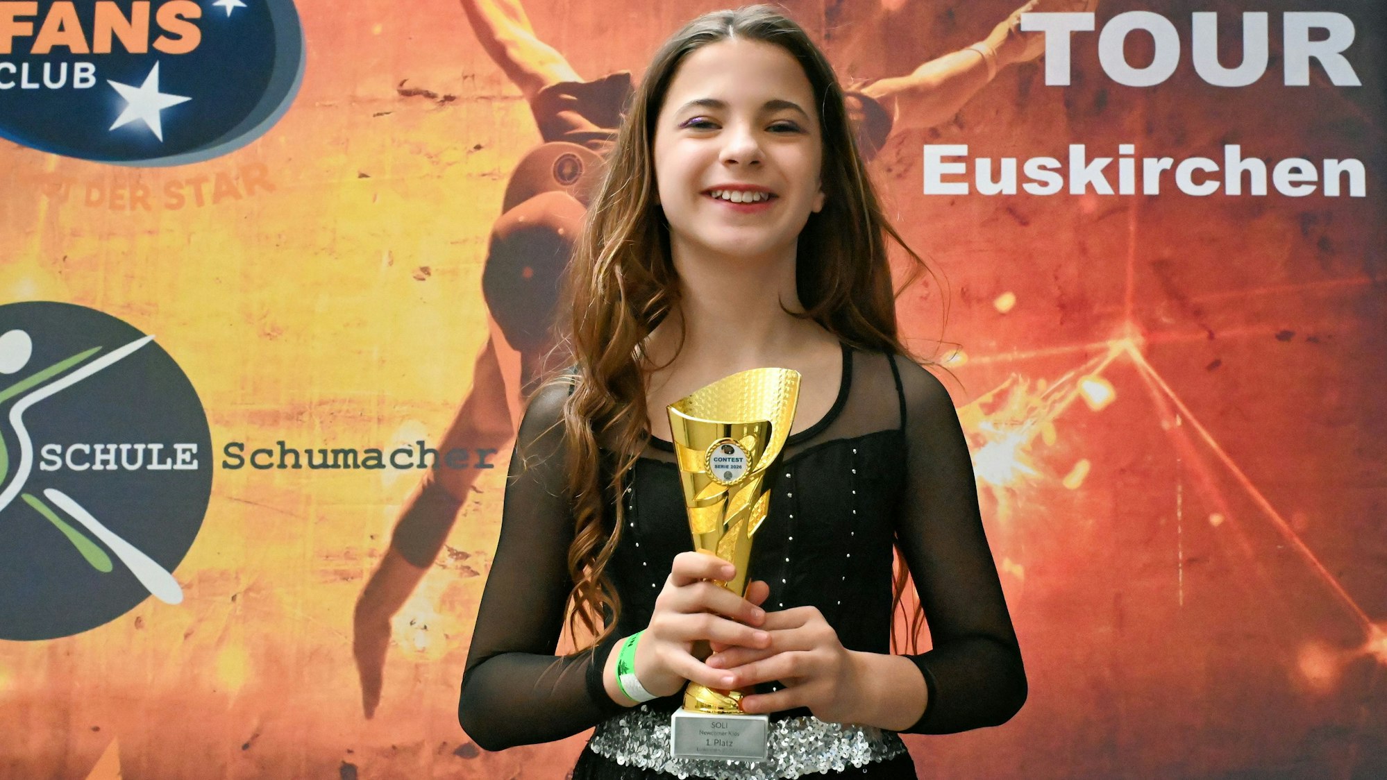 Das Mädchen vor einem Plakat und hält einen Pokal in den Händen.