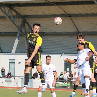 Mehrere Spieler versuchen, den Ball mit dem Kopf zu erreichen, andere beobachten die Szene..