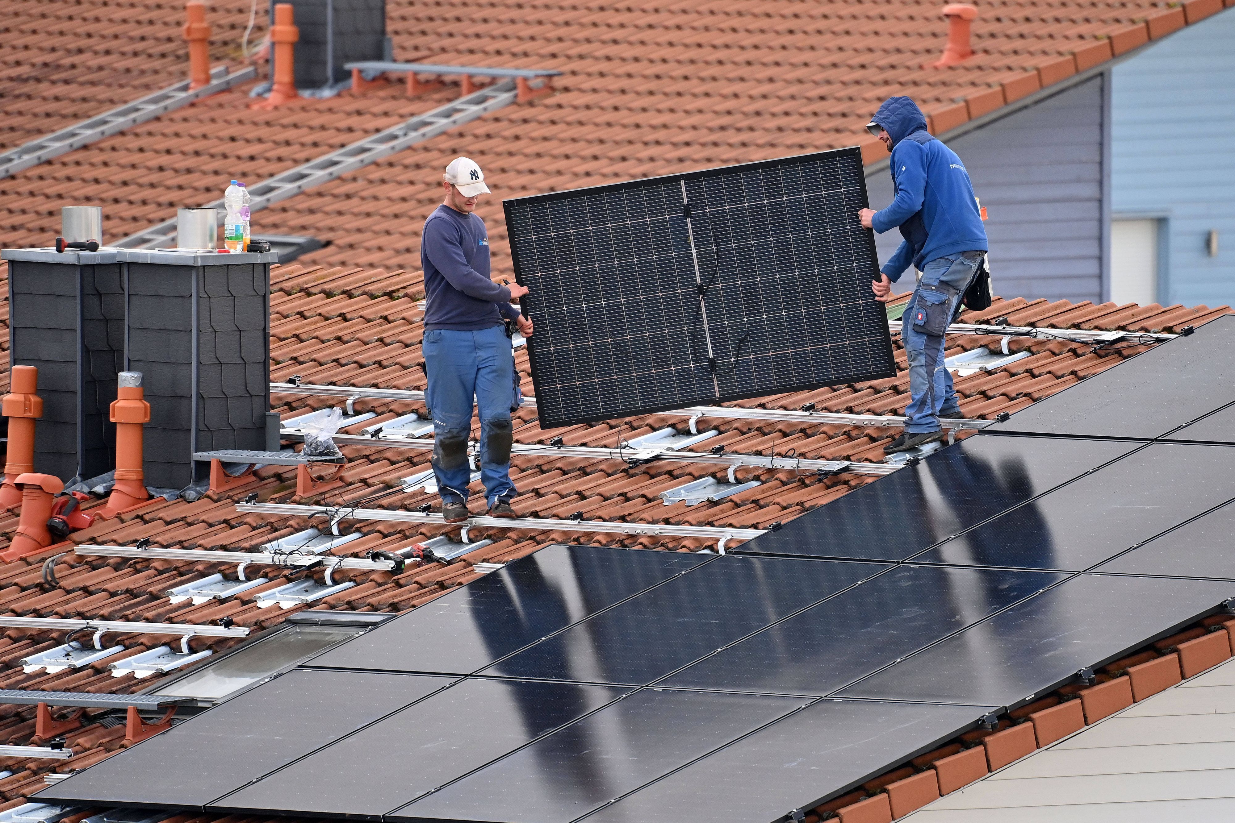 Arbeiter bei der Montage von Solarpanels auf einem Hausdach.