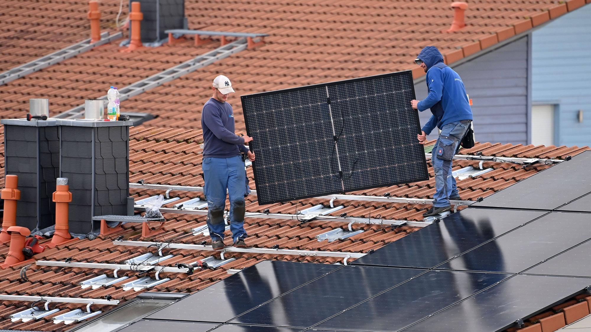 Arbeiter bei der Montage von Solarpanels auf einem Hausdach.