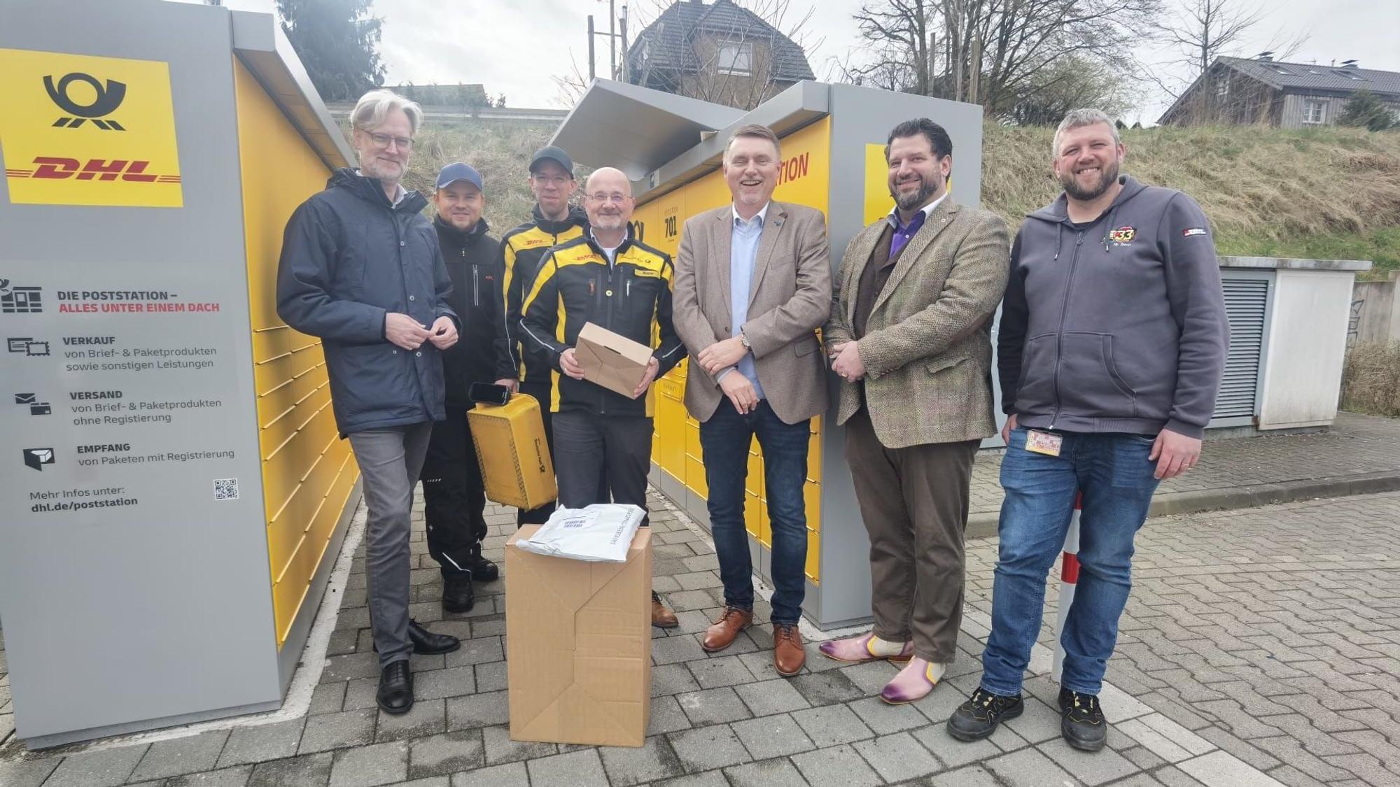 Eine Gruppe Männer steht vor einer DHL/Deutsche Post Packstation.