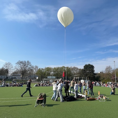 Jugendliche stehen auf einem Sportplatz um einen weißen Ballon herum.