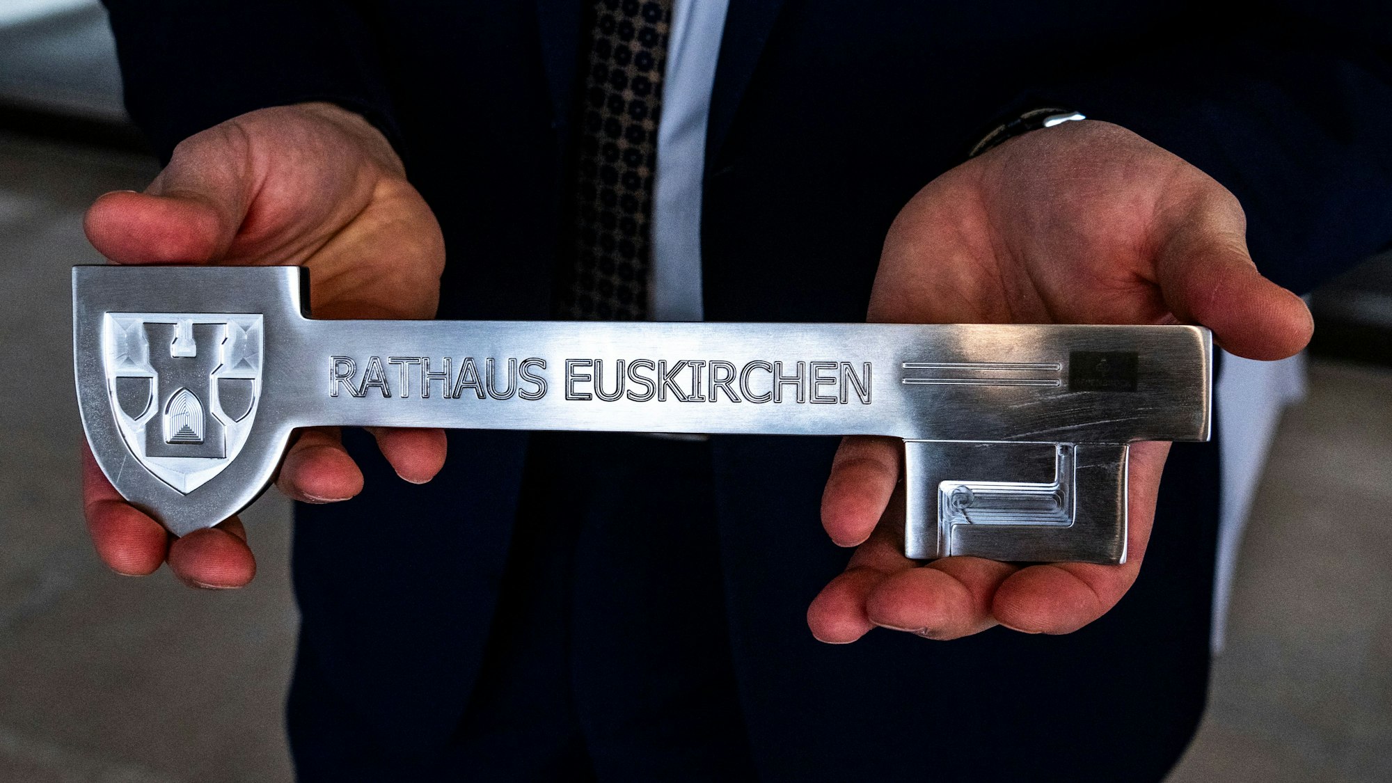 Zwei Hände halten einen überdimensionierten Schlssel, auf dem „Stadt Euskirchen“ steht.