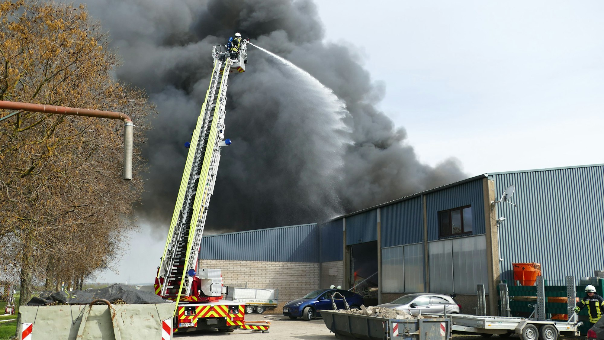 Drehleiter der Feuerwehr im Einsatz über einer brennenden Lagerhalle.