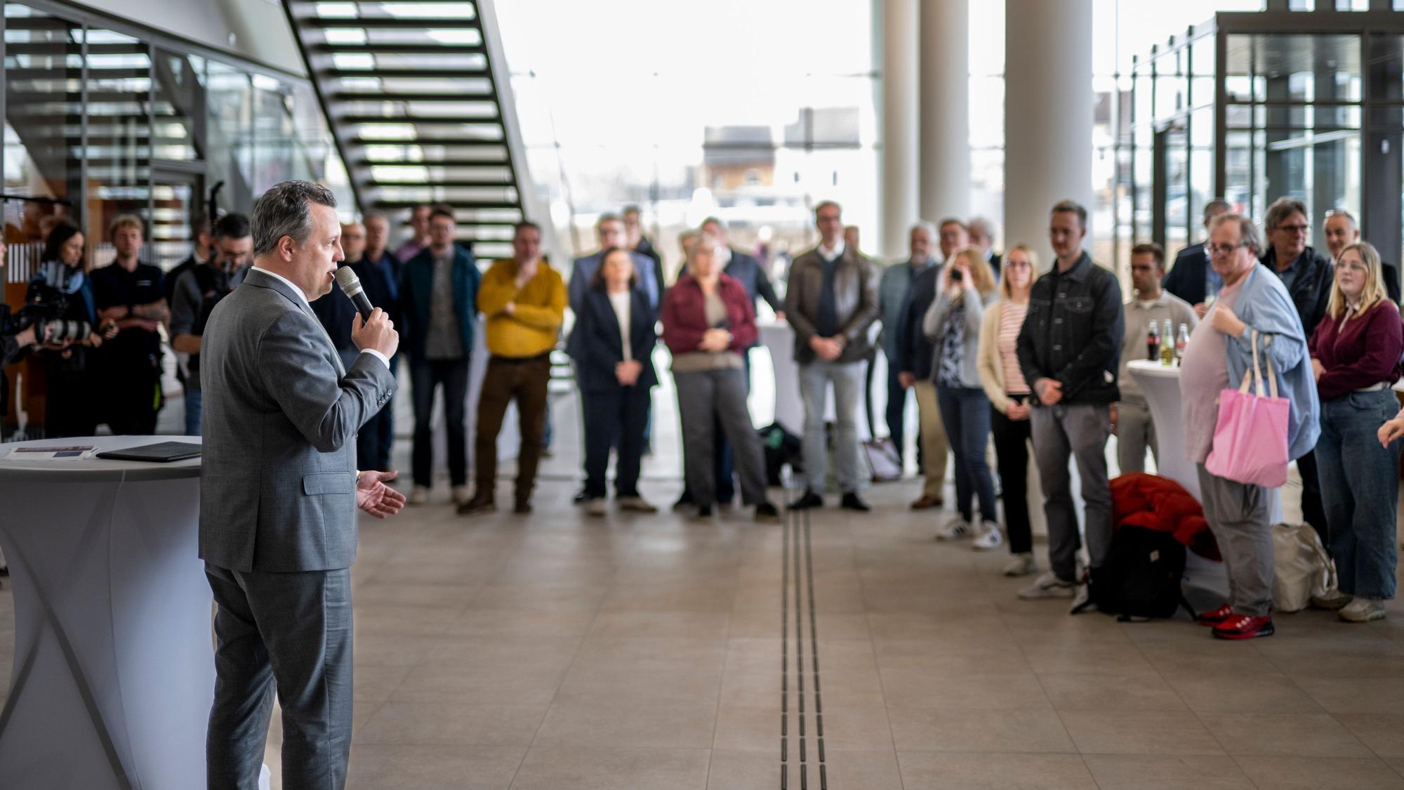Bürgermeister Sacha Reichelt steht vor einer Gruppe Menschen und spricht in ein Mikrofon.