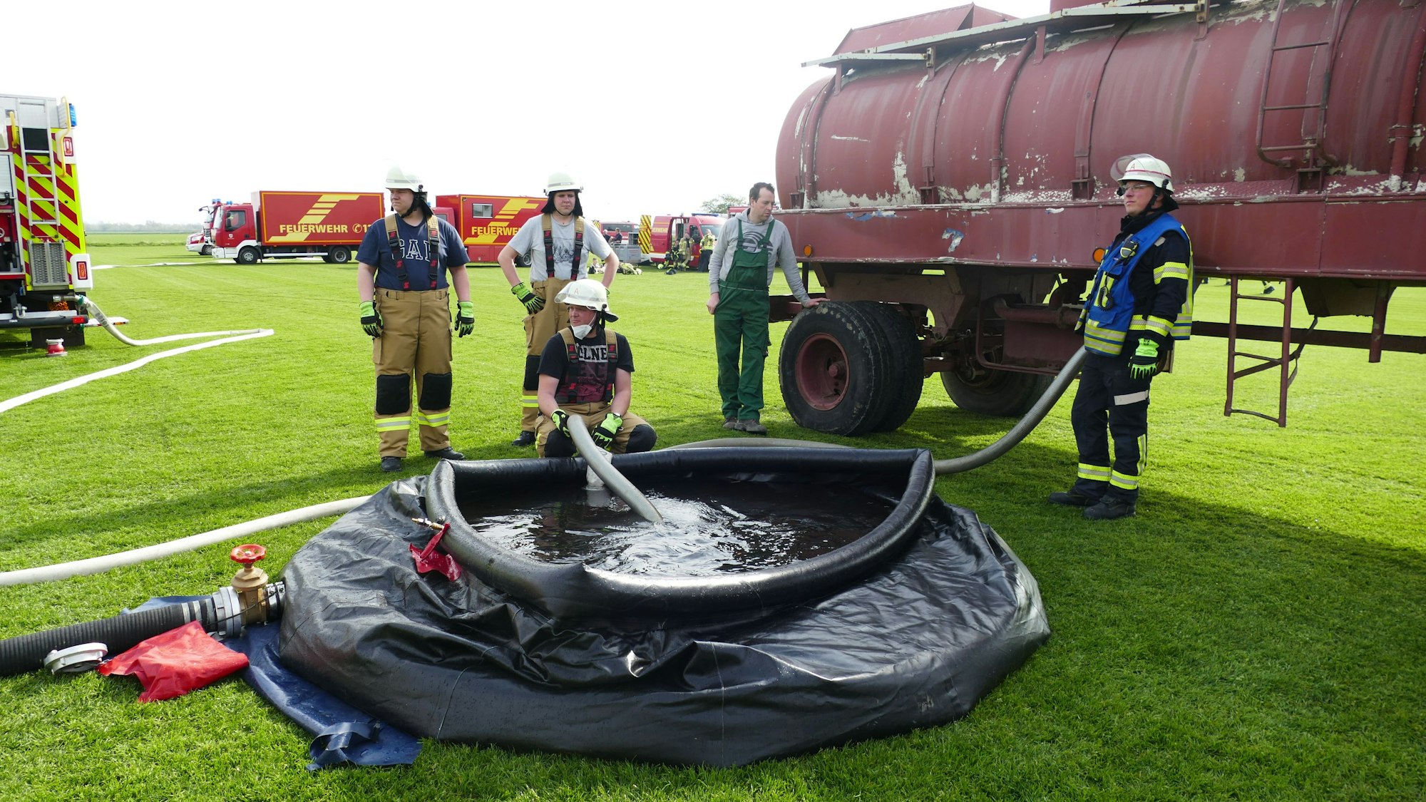 Feuerwehrleute füllen ein schwarzes Schlauchbecken mit Wasser aus einem Güllelaster.