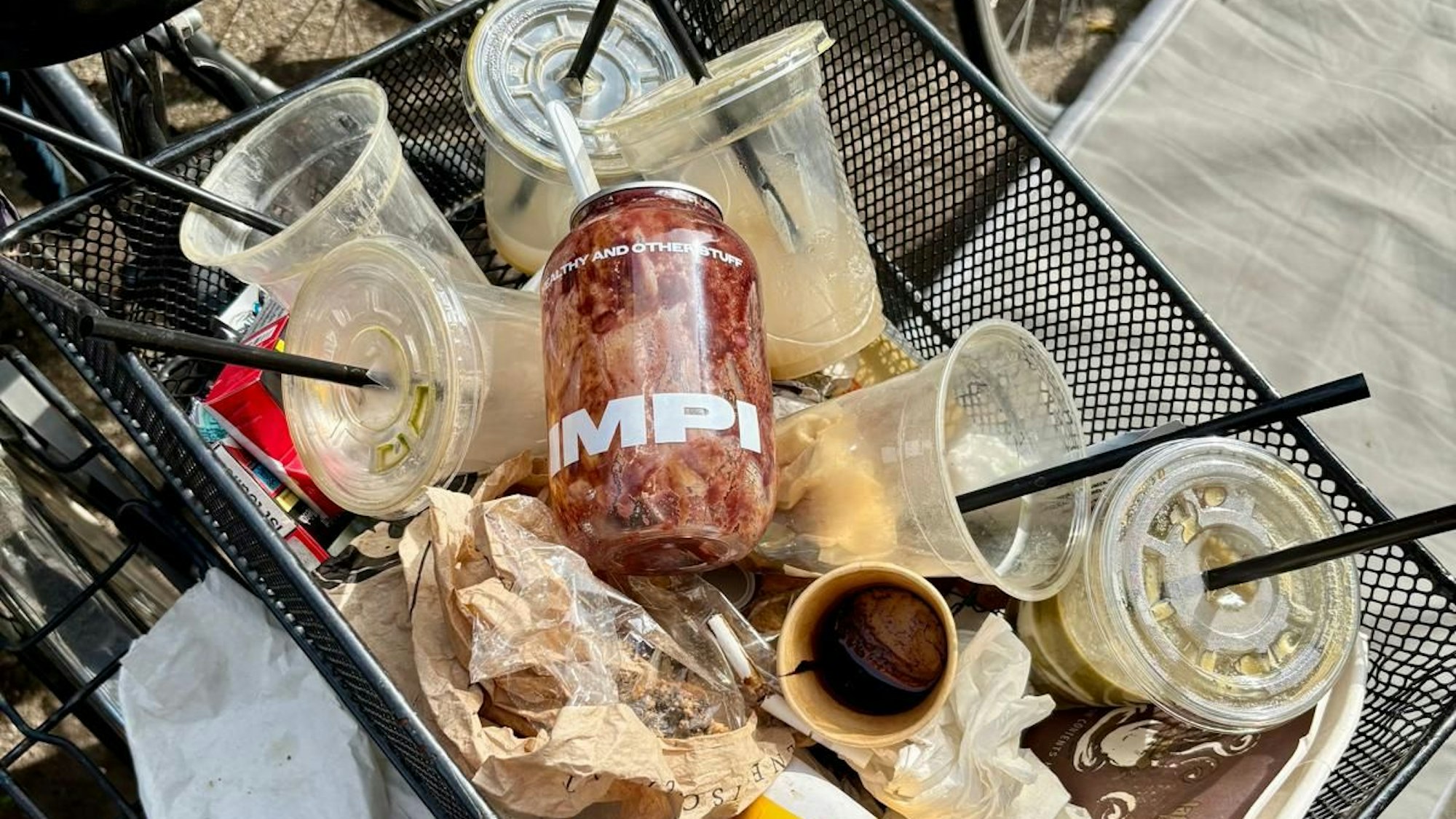 Ein Fahrradkorb ist voll mit leeren Getränkebechern aus Plastik.