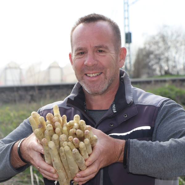 Das Foto zeigt den Landwirt mit einem Bündel Spargelstangen in den Händen auf einem der Felder.