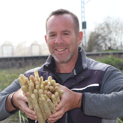 Das Foto zeigt den Landwirt mit einem Bündel Spargelstangen in den Händen auf einem der Felder.