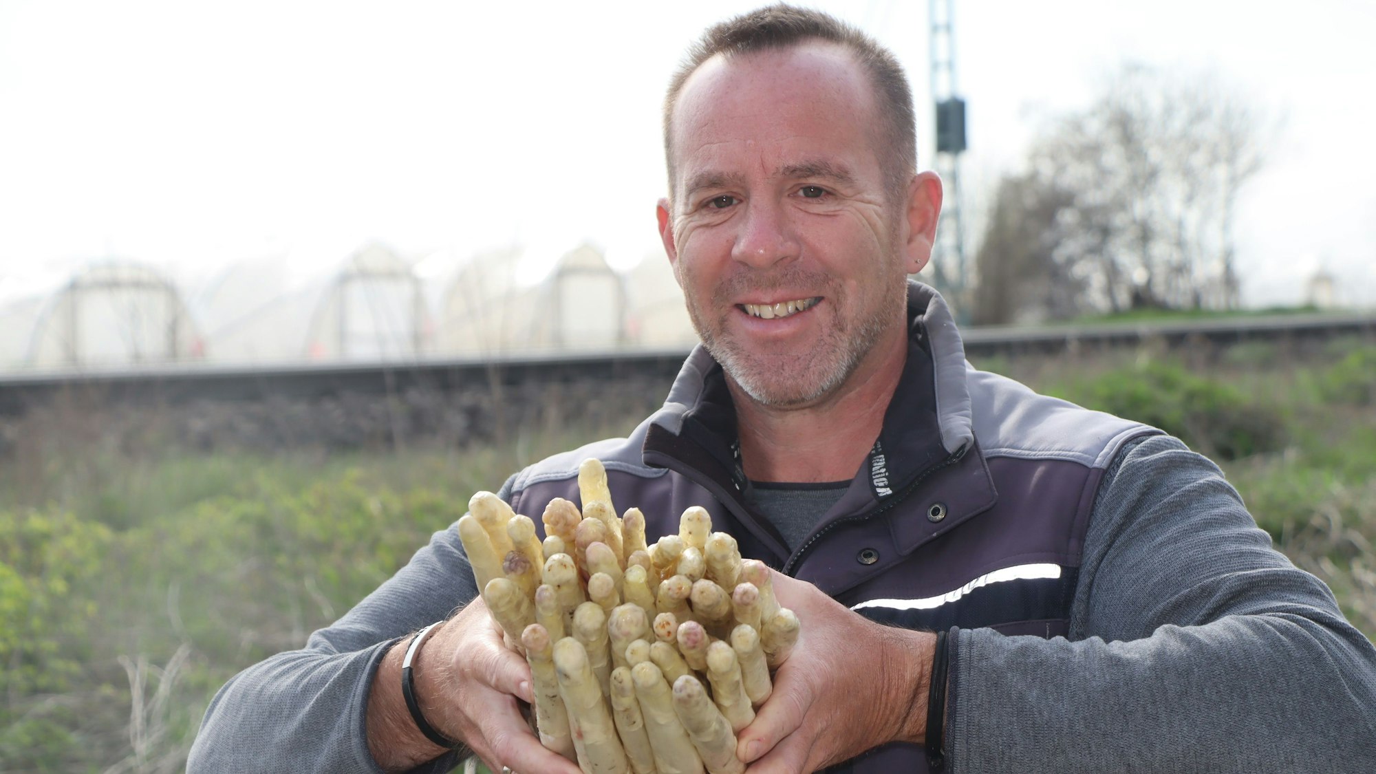 Das Foto zeigt den Landwirt mit einem Bündel Spargelstangen in den Händen auf einem der Felder.