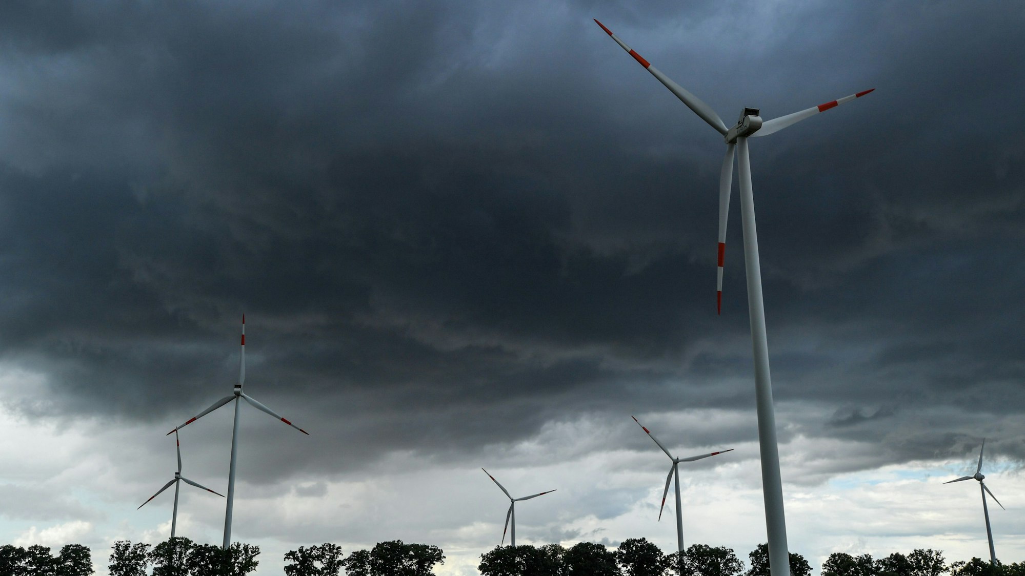Zu sehen sind dunkle Wolken am Himmel über mehreren Windrädern