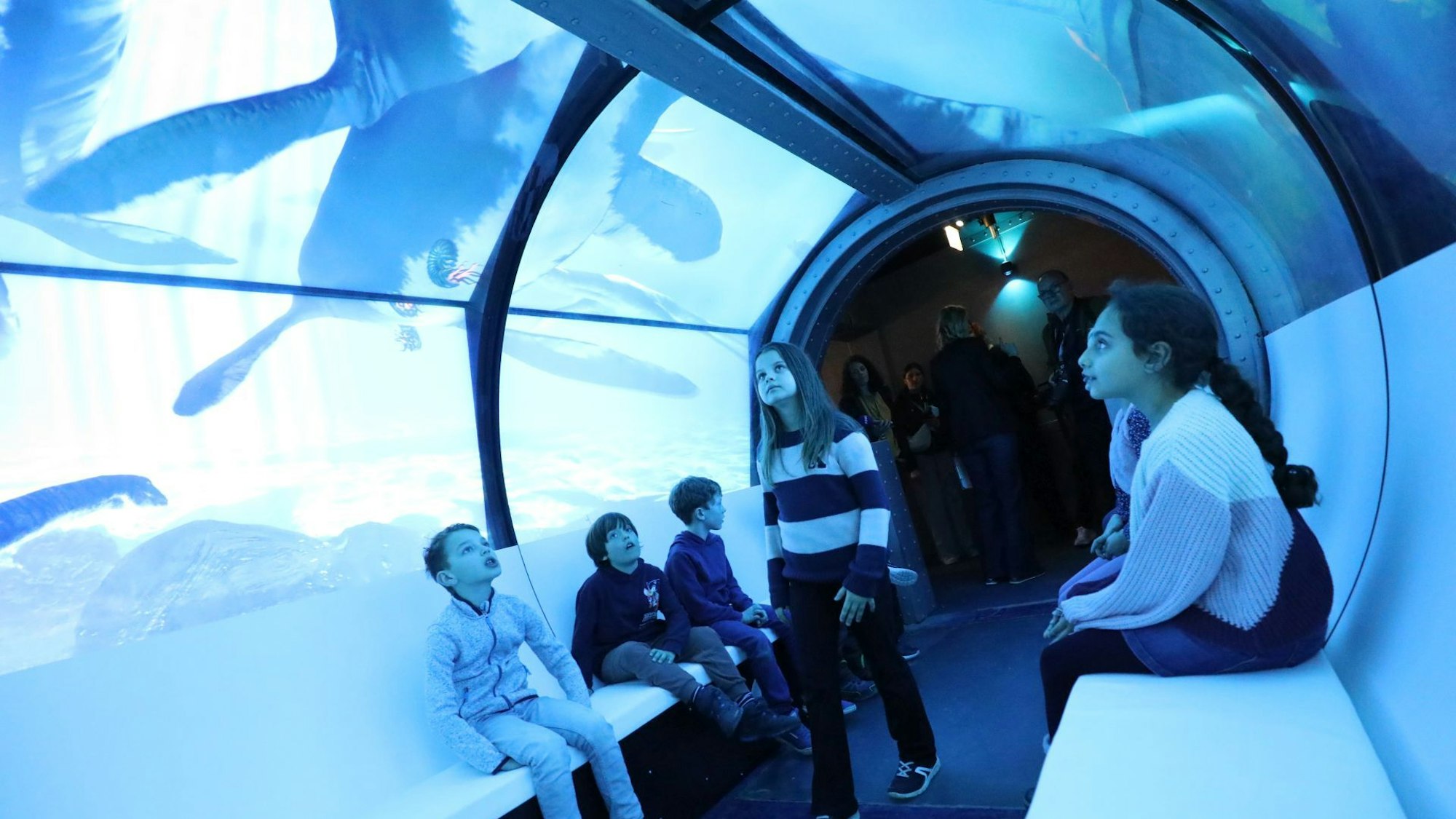 Kinder in einem Glastunnel, auf und über den Bilder von Dinosauriern projiziert werden.