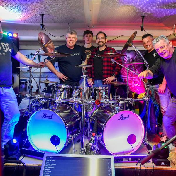 Auf dem Bild sind die Musiker der Frechener Band Electrified zu sehen, die im Proberaum um ein Schlagzeug versammelt sind.