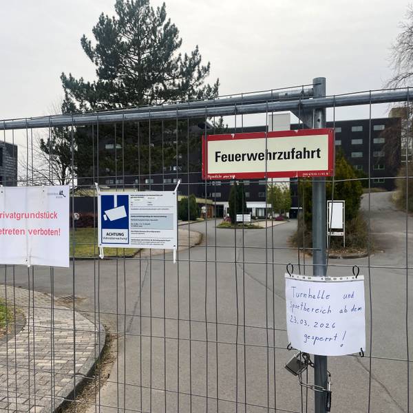 Das Gelände der ehemaligen Eifelhöhen-Klinik ist mit einem Zaun abgesperrt, an dem mehrere Schilder befestigt sind.