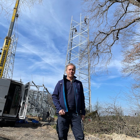 Ein Mann steht in blauer Funktionskleidung vor dem Aufbau eines Sendemasts.